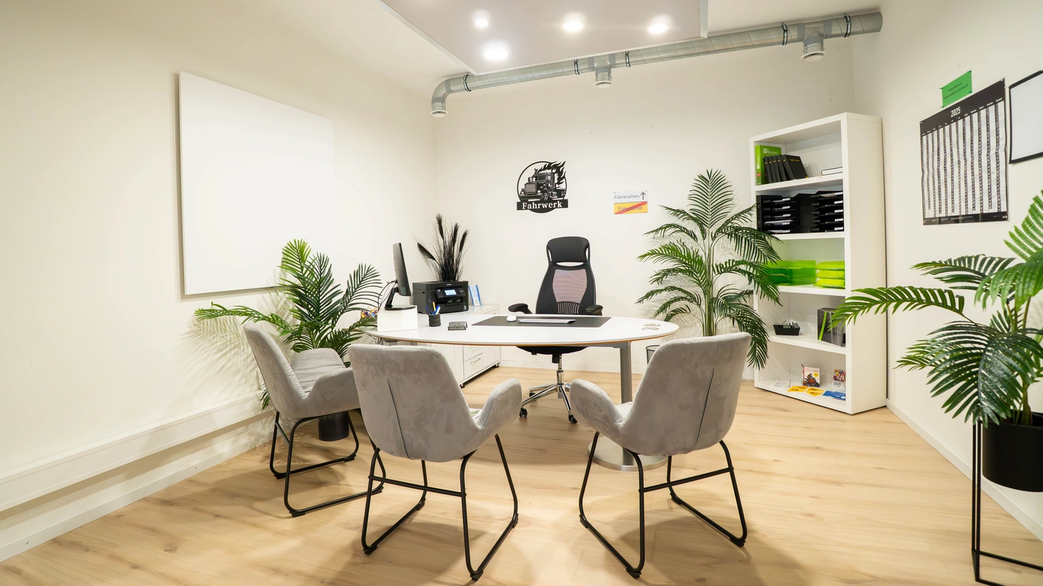 Fahrschule Fahrwerk Bayer GmbH - Führerscheinausbildung - Ein modernes, helles Fahrschulklassenzimmer mit weißen Tischen, Stühlen und Pflanzen.