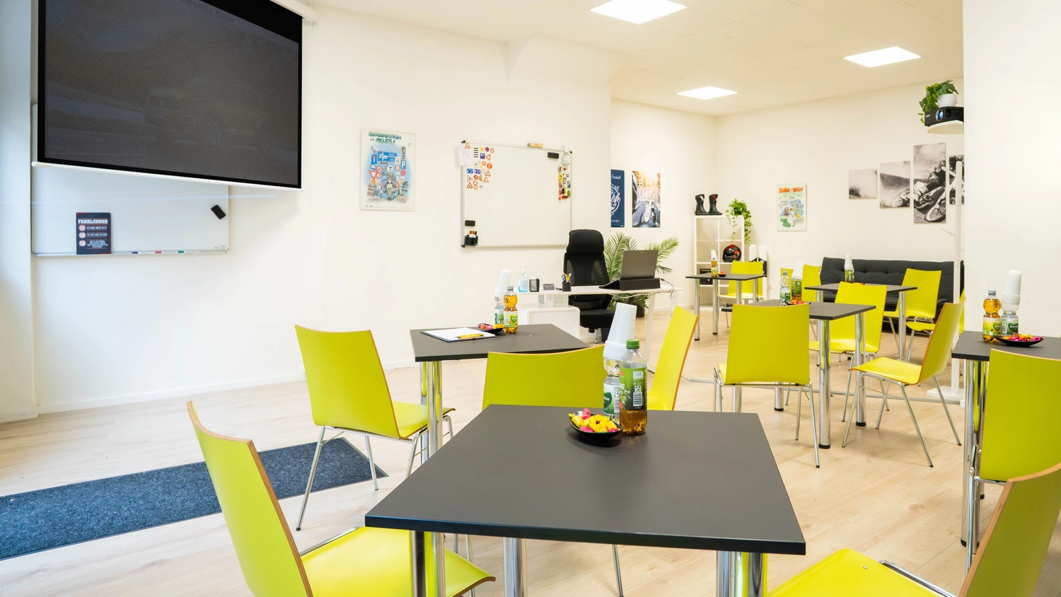 Fahrschule Fahrwerk Bayer GmbH - Führerscheinausbildung - Ein Klassenzimmer oder Bürobereich mit gelben und schwarzen Stühlen, einem Tisch und einem an der Wand montierten Fernseher.