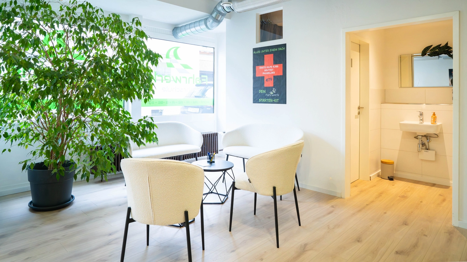 Eine Sitzecke mit zwei weißen Stühlen und einer großen Topfpflanze, daneben ein Poster an der Wand.