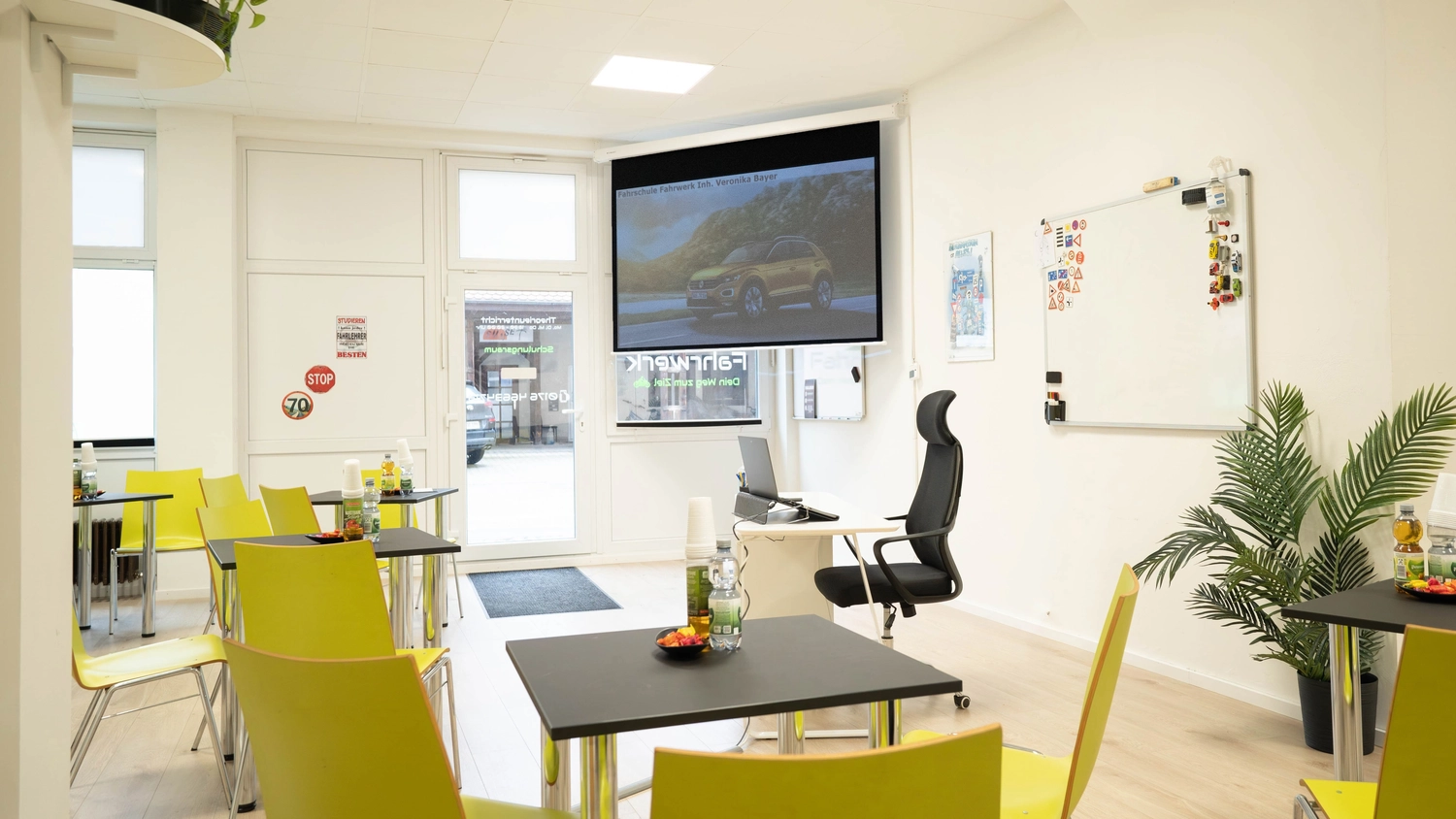 Fahrschule Fahrwerk Bayer GmbH - Führerscheinausbildung - Eine andere Ansicht eines modernen Fahrschulklassenzimmers mit gelben Stühlen und einem großen Bildschirm.