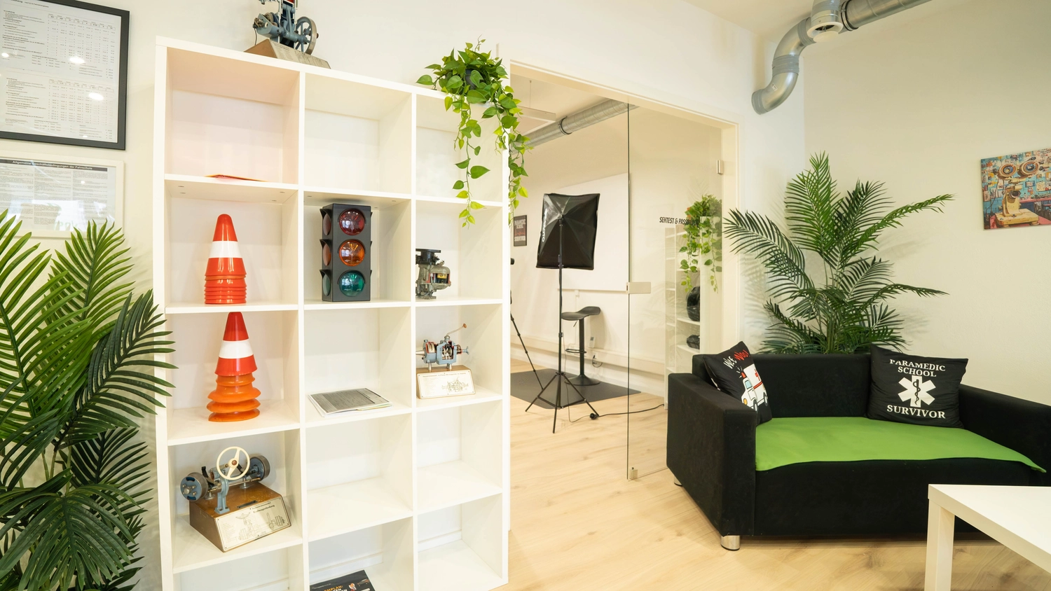 Fahrschule Fahrwerk Bayer GmbH - Führerscheinausbildung - Ein moderner Wartebereich mit schwarzen Sofas, weißen Couchtischen, grünen Akzenten und Pflanzen.