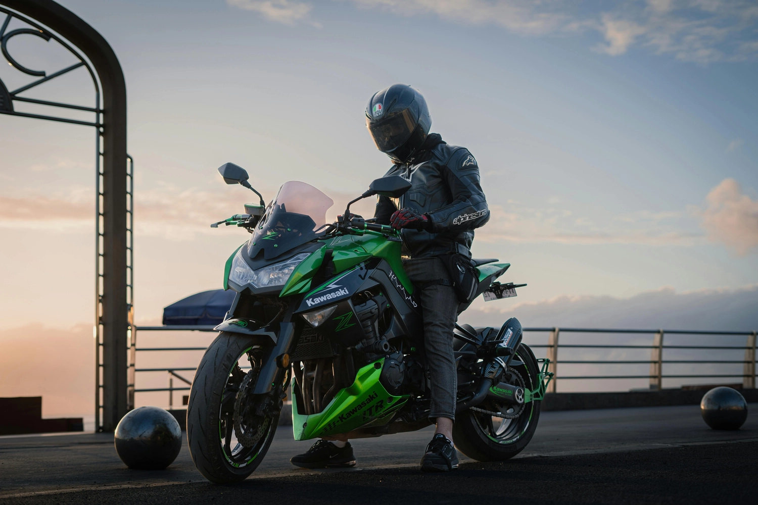 Fahrschule Fahrwerk Bayer GmbH - Führerscheinausbildung - Eine Person mit schwarzem Helm und grüner Jacke fährt auf einem grünen Kawasaki-Motorrad über eine Brücke.
