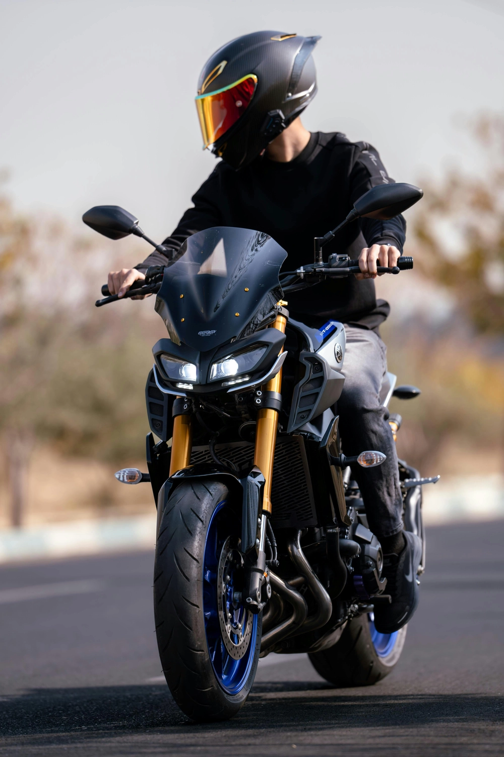 Nahaufnahme einer Person in schwarzer Jacke und schwarzem Helm mit rotem Visier, die auf einem schwarzen Motorrad sitzt.